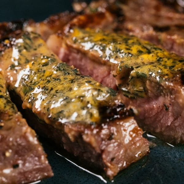 Close-up of sliced steak with a yellow-green sauce, showcasing its juicy interior and charred exterior.