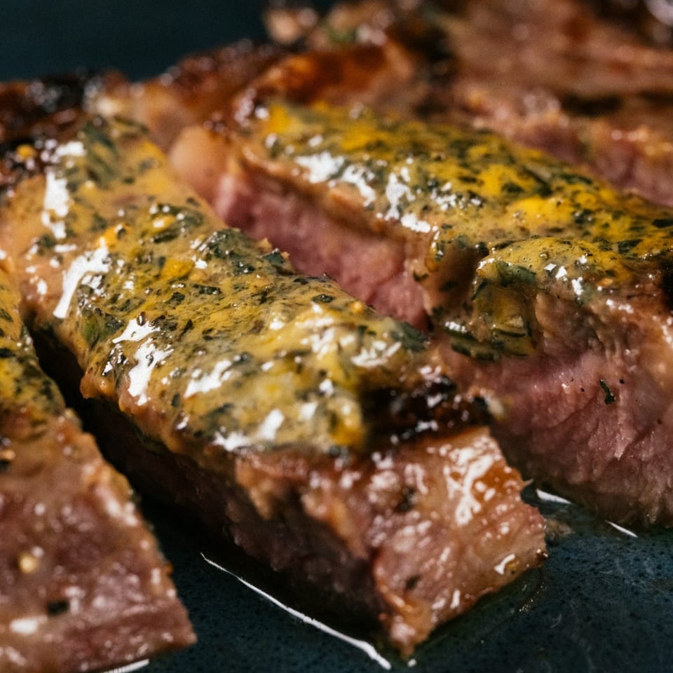 Close-up of sliced steak with a yellow-green sauce, showcasing its juicy interior and charred exterior.