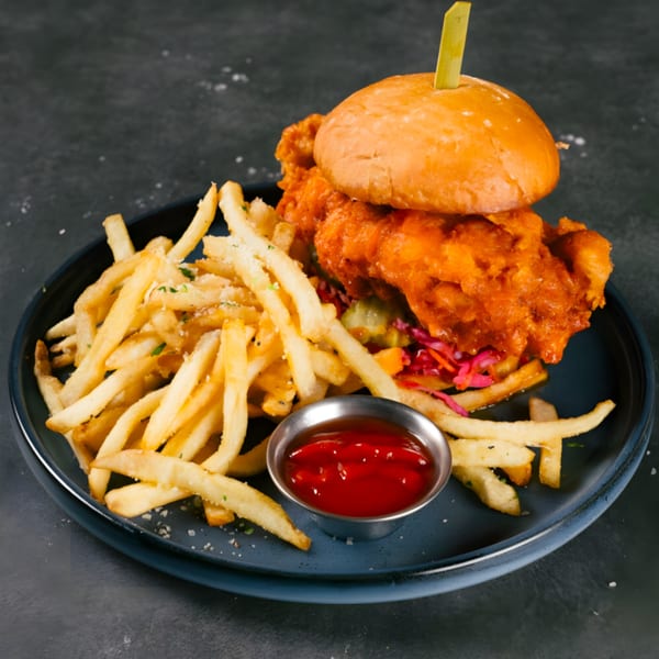 The Operators Club's crispy chicken sandwich with fries and ketchup on a dark plate.
