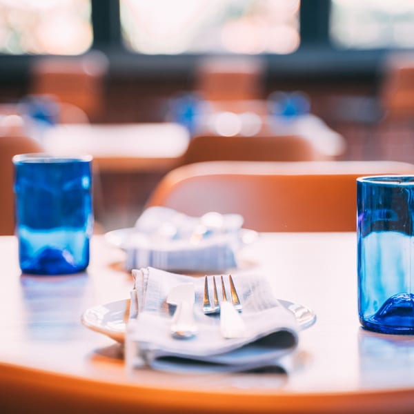 A set table at The Operators Club with blue glasses, white plates, and silverware on napkins.
