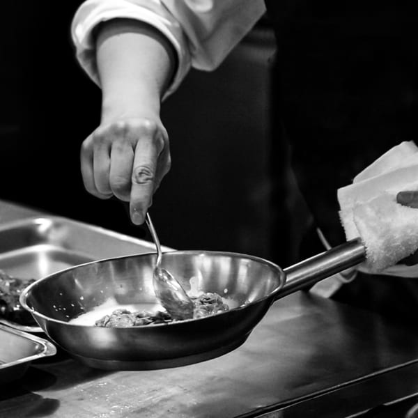 A chef in black and white stirs food in a pan with a spoon at The Operators Club.