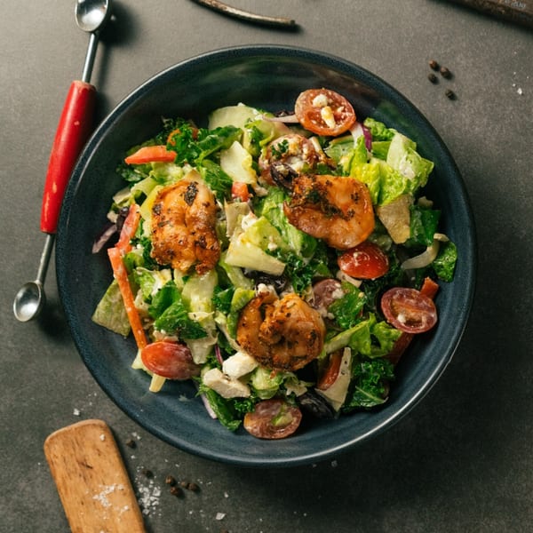A vibrant salad with grilled shrimp, mixed greens, cherry tomatoes, and feta cheese in a dark bowl.