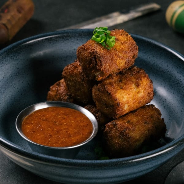 Crispy golden-brown tater tots, topped with green onions, served with a side of dipping sauce.